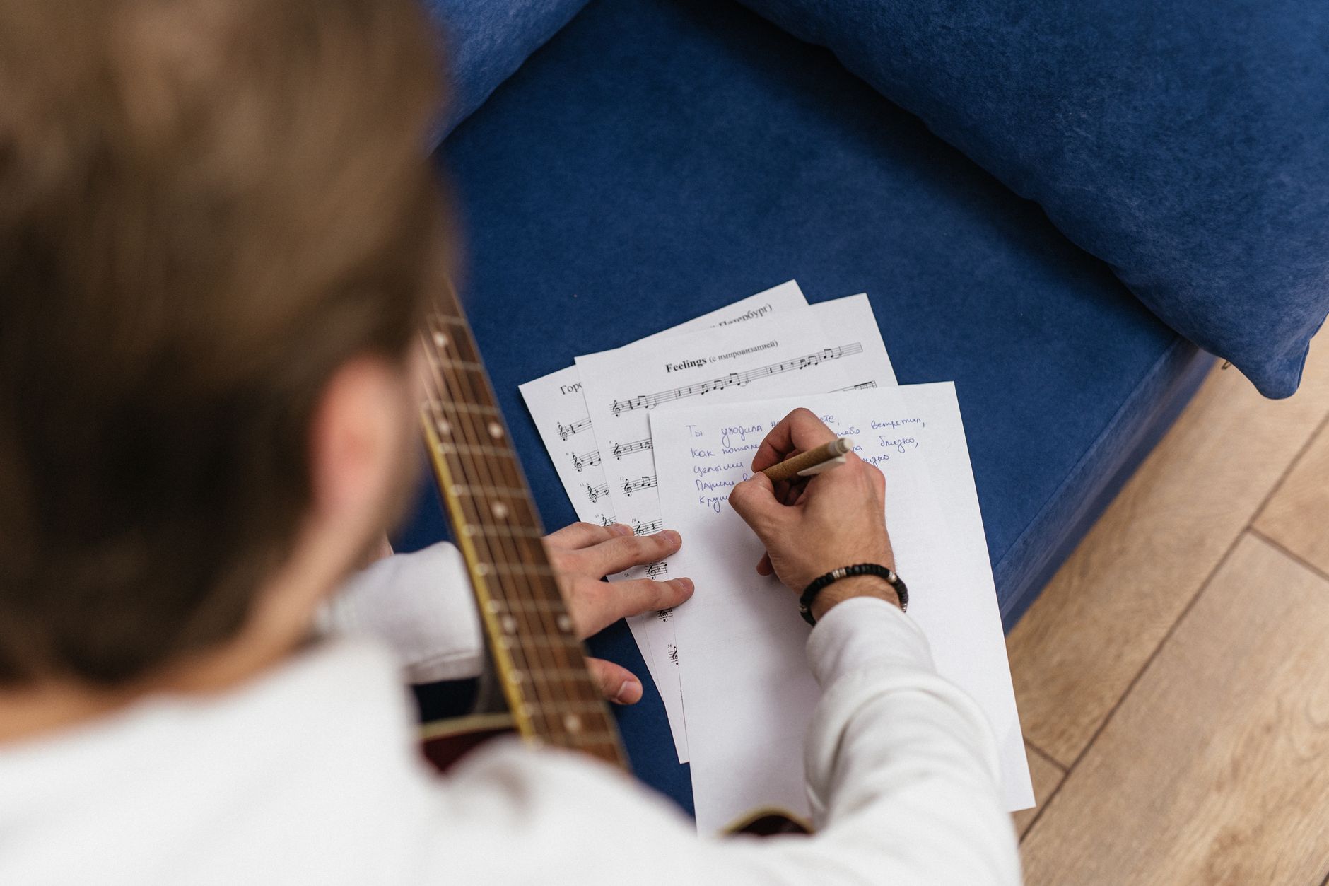 Man composing music on acoustic guitar with handwritten notes indoors.