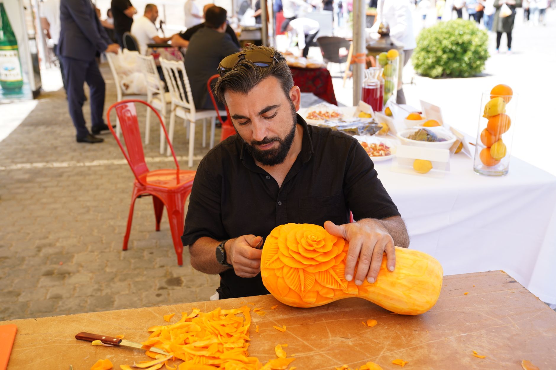 A talented artist carves a detailed floral design into a pumpkin at an outdoor event.
