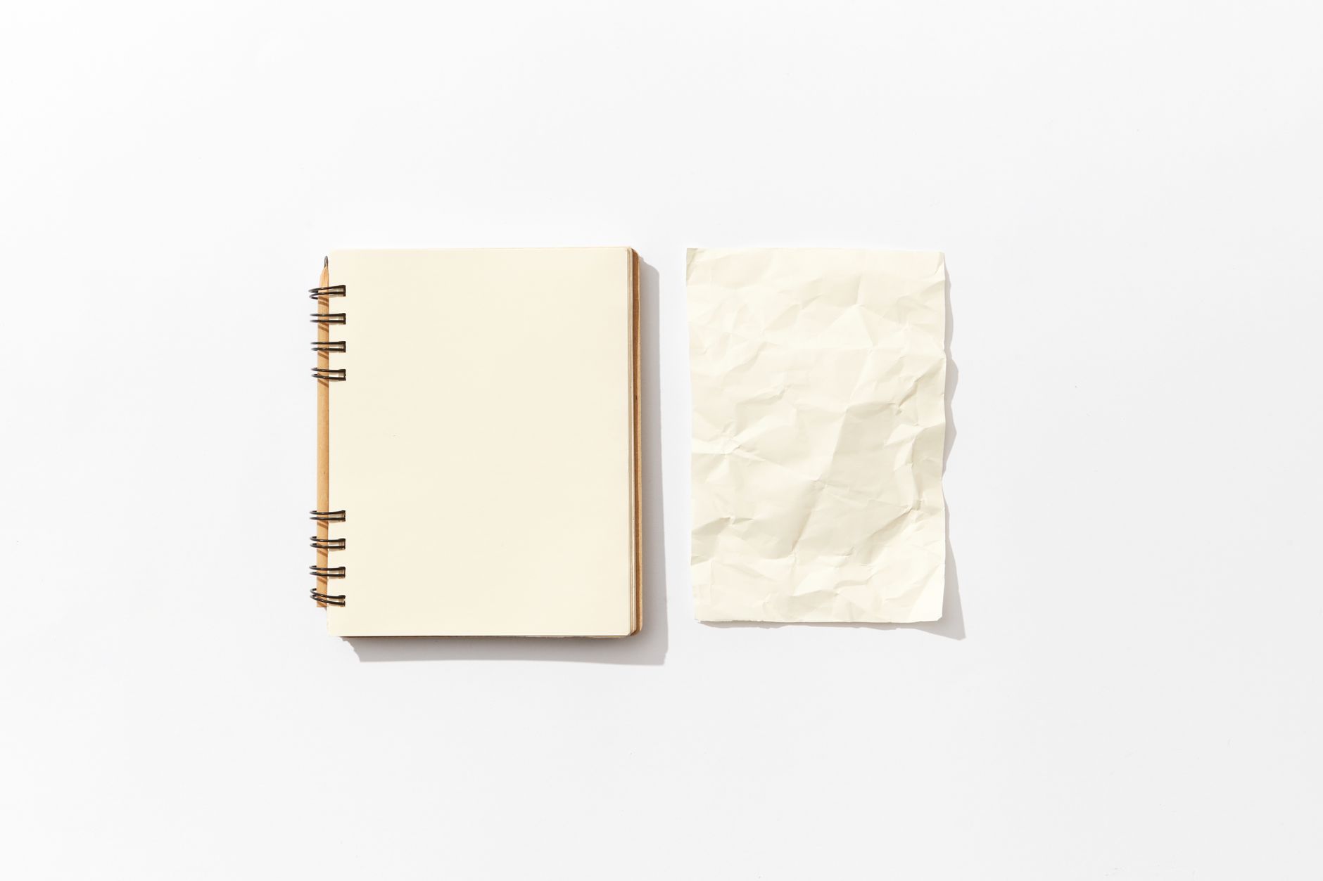 Flat lay of an open spiral notebook and a crumpled paper on a white background, perfect for mockup designs.