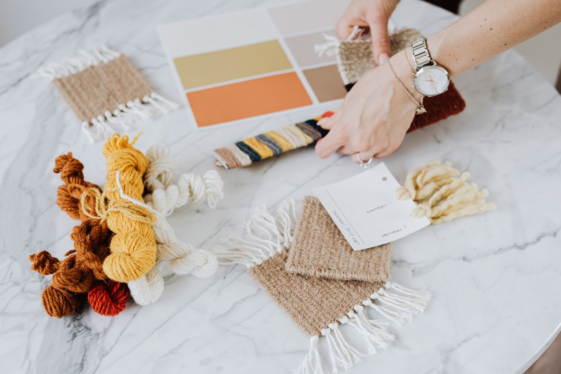 Close-up of hands working with yarn and textile samples on a marble table.