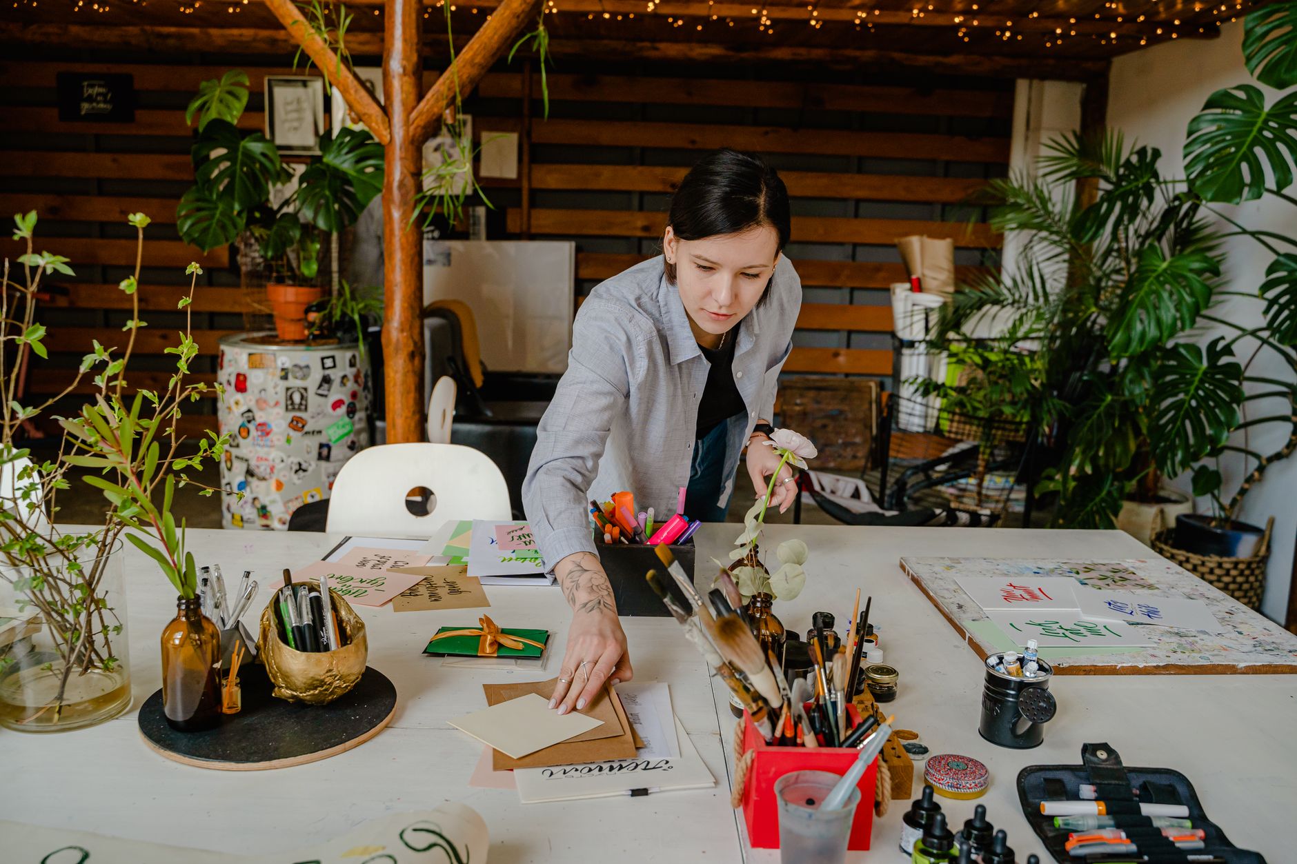 A woman organizing art supplies on a desk in a creatively decorated indoor workspace.