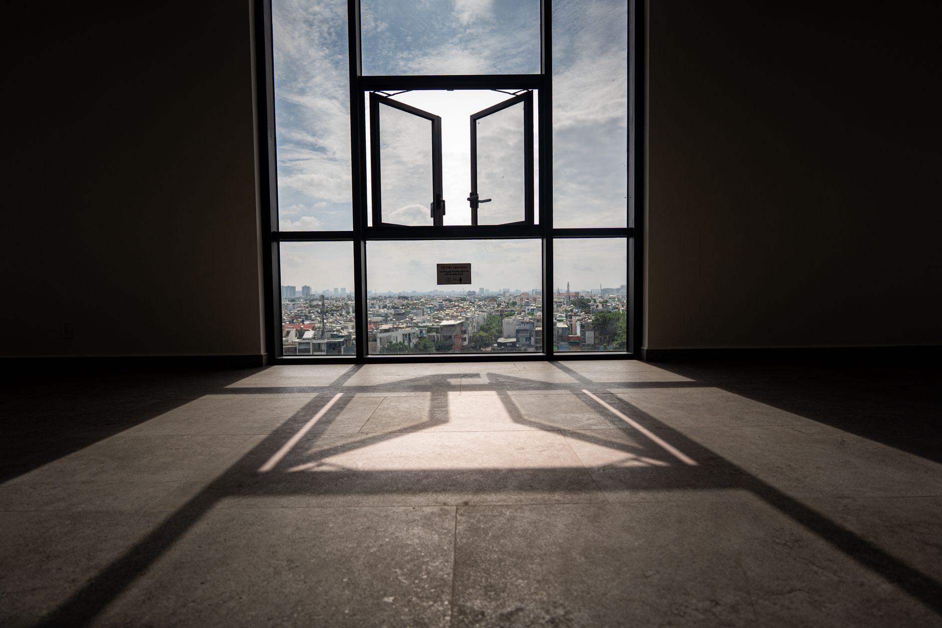 Sunlit room with open window framing a panoramic urban landscape view.