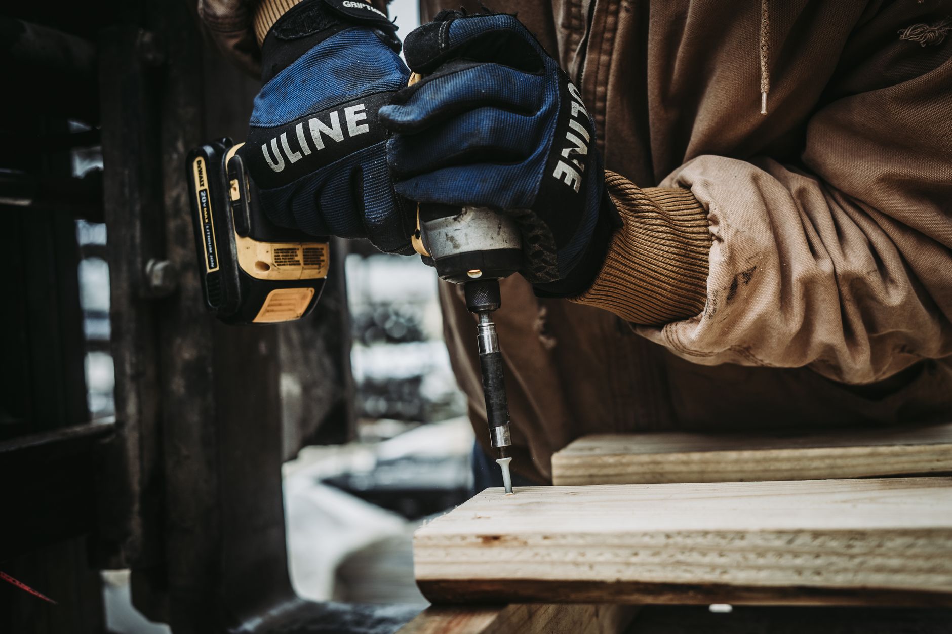 Carpenter uses power drill in a workshop setting, close-up with focus on hands and tool.