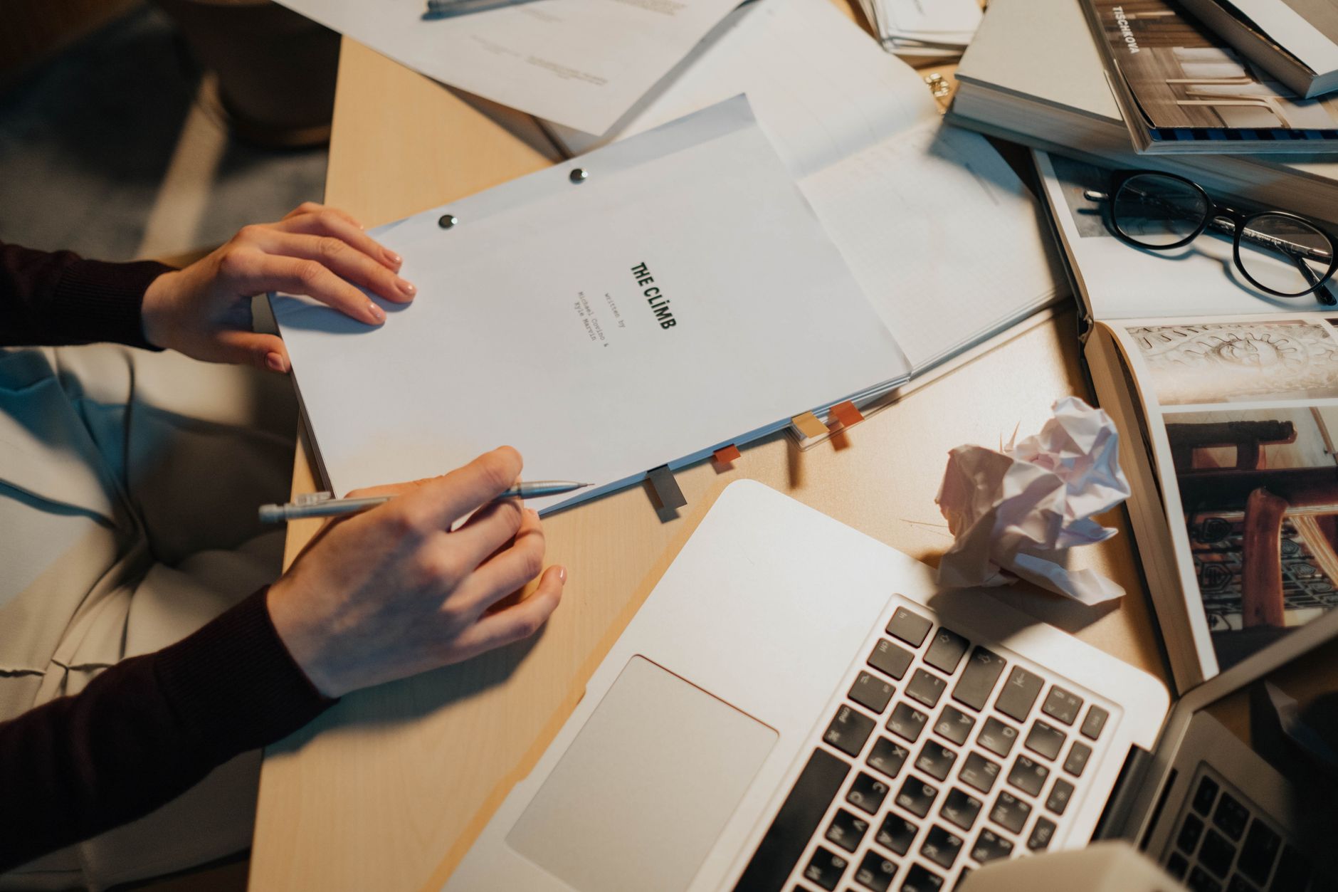 Mains tenant un scénario relié et un crayon au-dessus d'un bureau avec ordinateur portable et lunettes