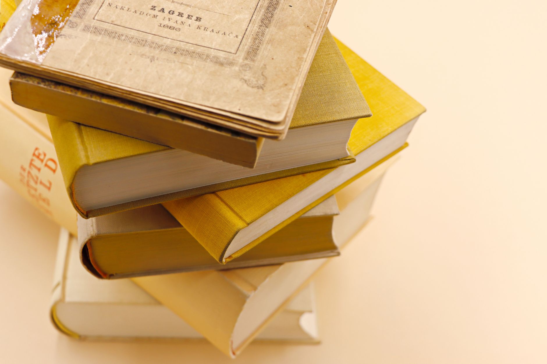 Pile de livres anciens aux couvertures jaunes et crème, l'un portant le mot Zagreb, sur un fond beige