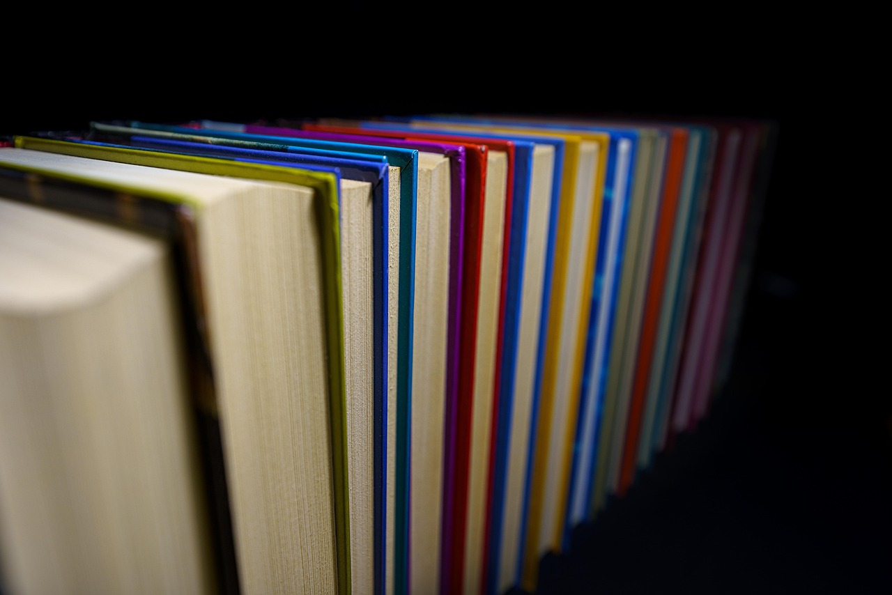 Rangée de livres aux couvertures colorées vus par la tranche avant, sur fond noir